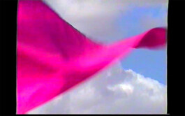A bright pink flag that is part of the textile installation path mark 07/22 by Isabelle Lange fluttering against a backdrop of a clear blue sky with sparse white clouds. ISO LA - Isabelle Lange