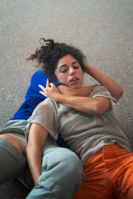 The performer Luisa Saraiva with curly hair wearing a mesh sweater during the performance Tirana, wearing a costume by Isabelle Lange. ISO LA - Isabelle Lange