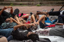 A group of young people lie on their backs on blankets outdoors, participating in the performance Tributary in a public square. ISO LA - Isabelle Lange